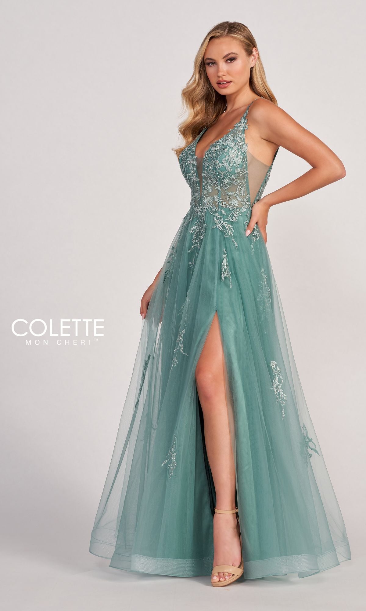 A woman wears the CL2074 Tulle A-Line Prom Dress featuring a sleeveless design, sheer bodice, deep V-neckline, floral embroidery, lace appliques, and a thigh-high slit. She poses against a plain background.